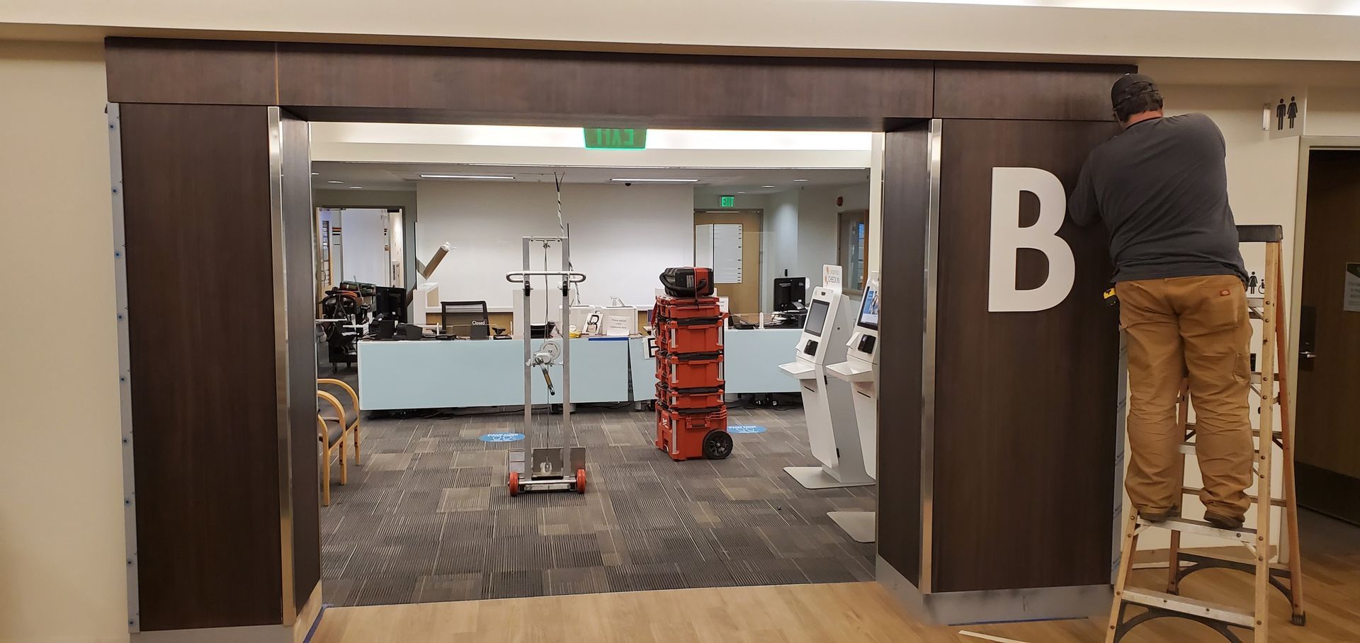 Gym entrance with a large “B” sign, a ladder, and exercise equipment visible inside.