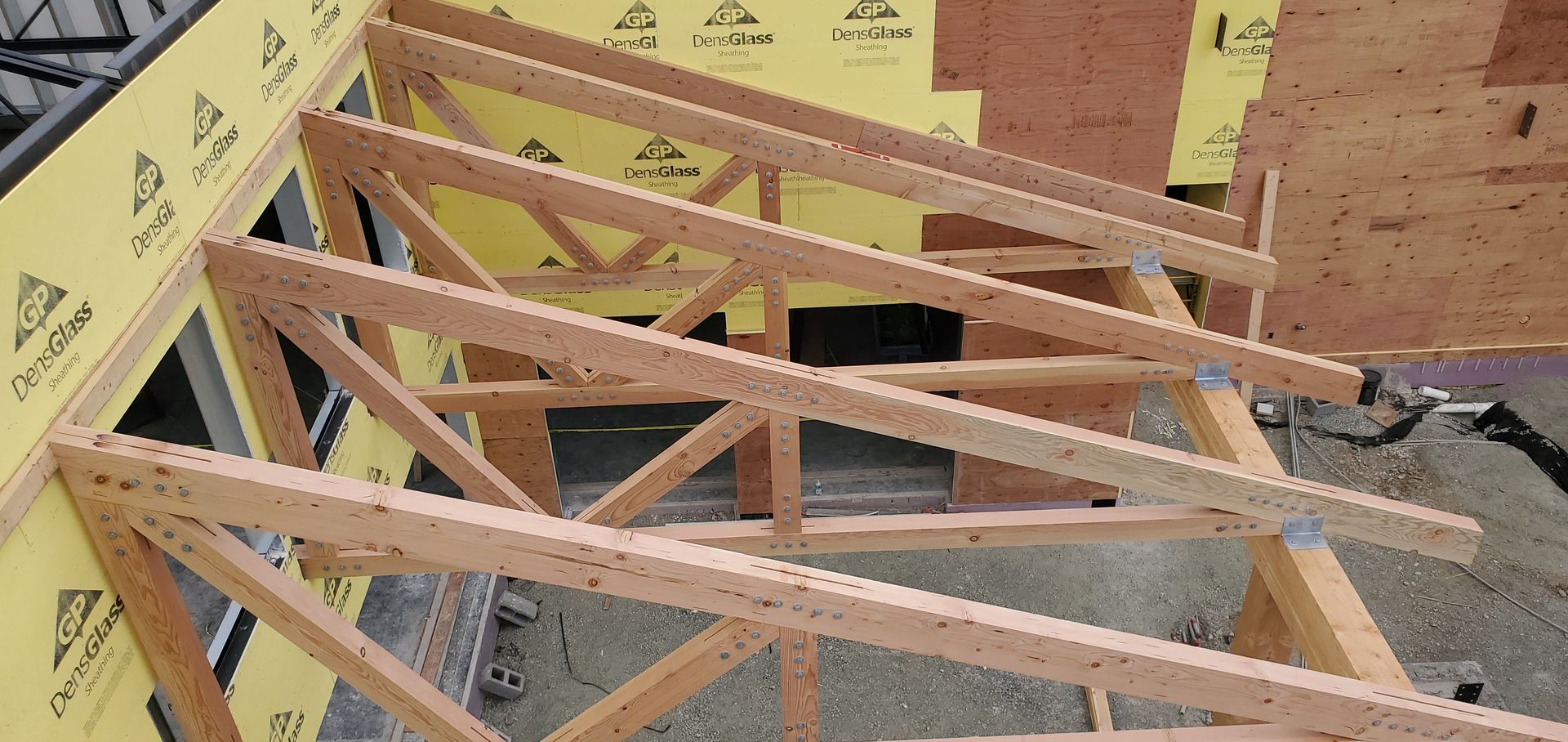 Wooden roof trusses under construction on a house frame, with yellow sheathing and plywood decking visible