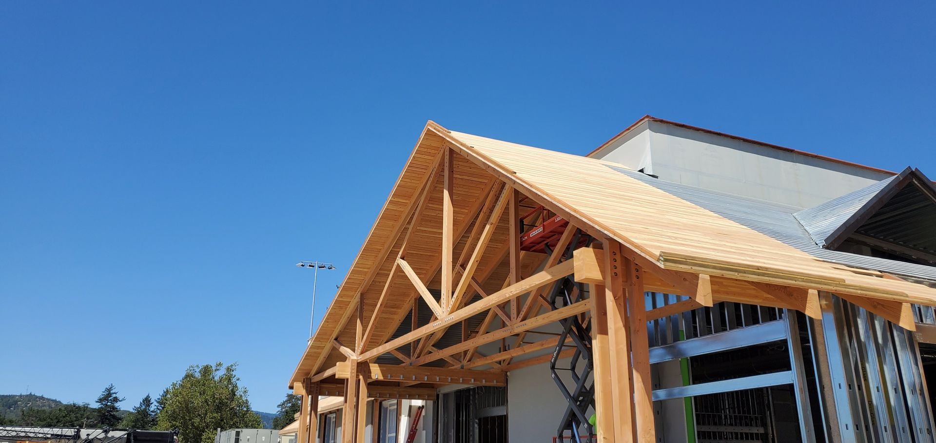 Wooden building under construction with exposed roof trusses against a clear blue sky