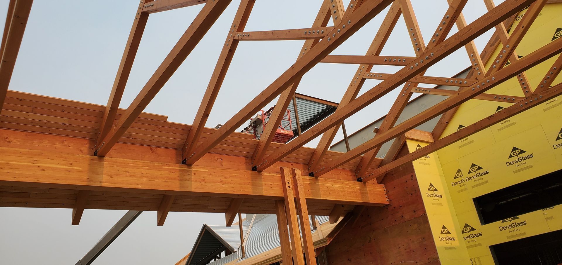 Wooden roof trusses over a building frame, with yellow protective sheeting on the right side.