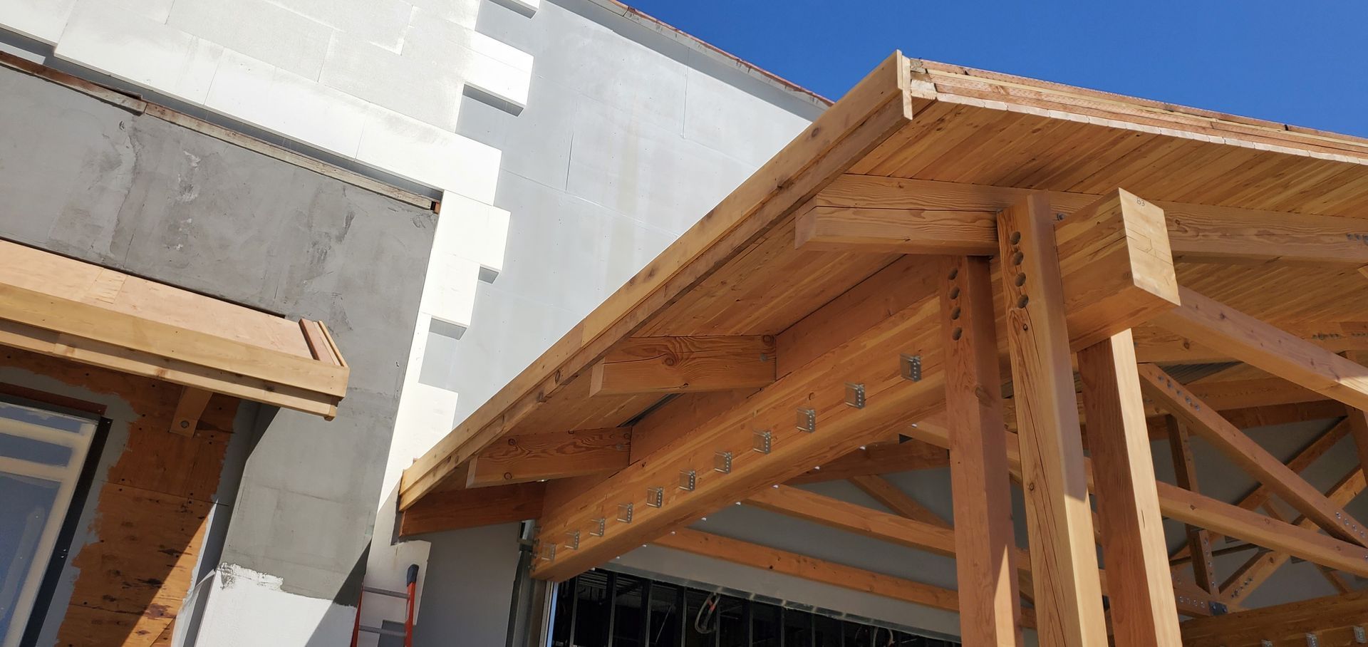 Wooden roof framing on a building under construction beside a white exterior wall
