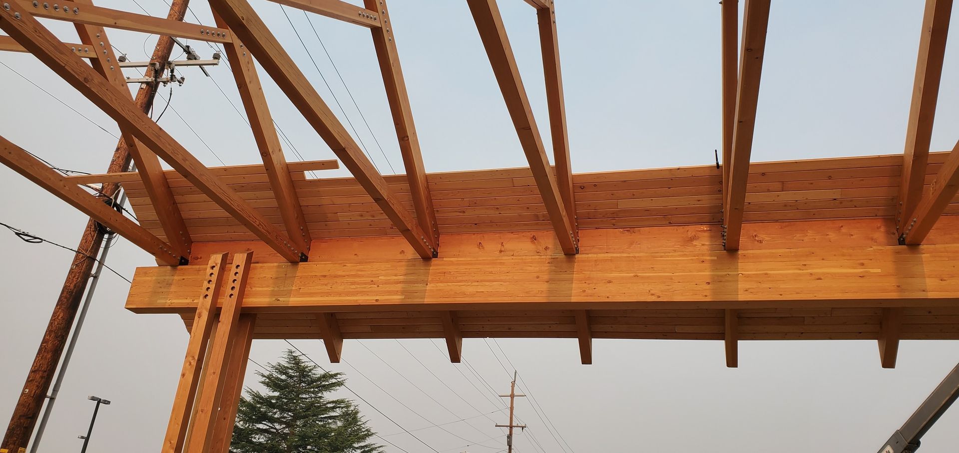 Partially built wooden roof frame over a building, viewed from below against a cloudy sky