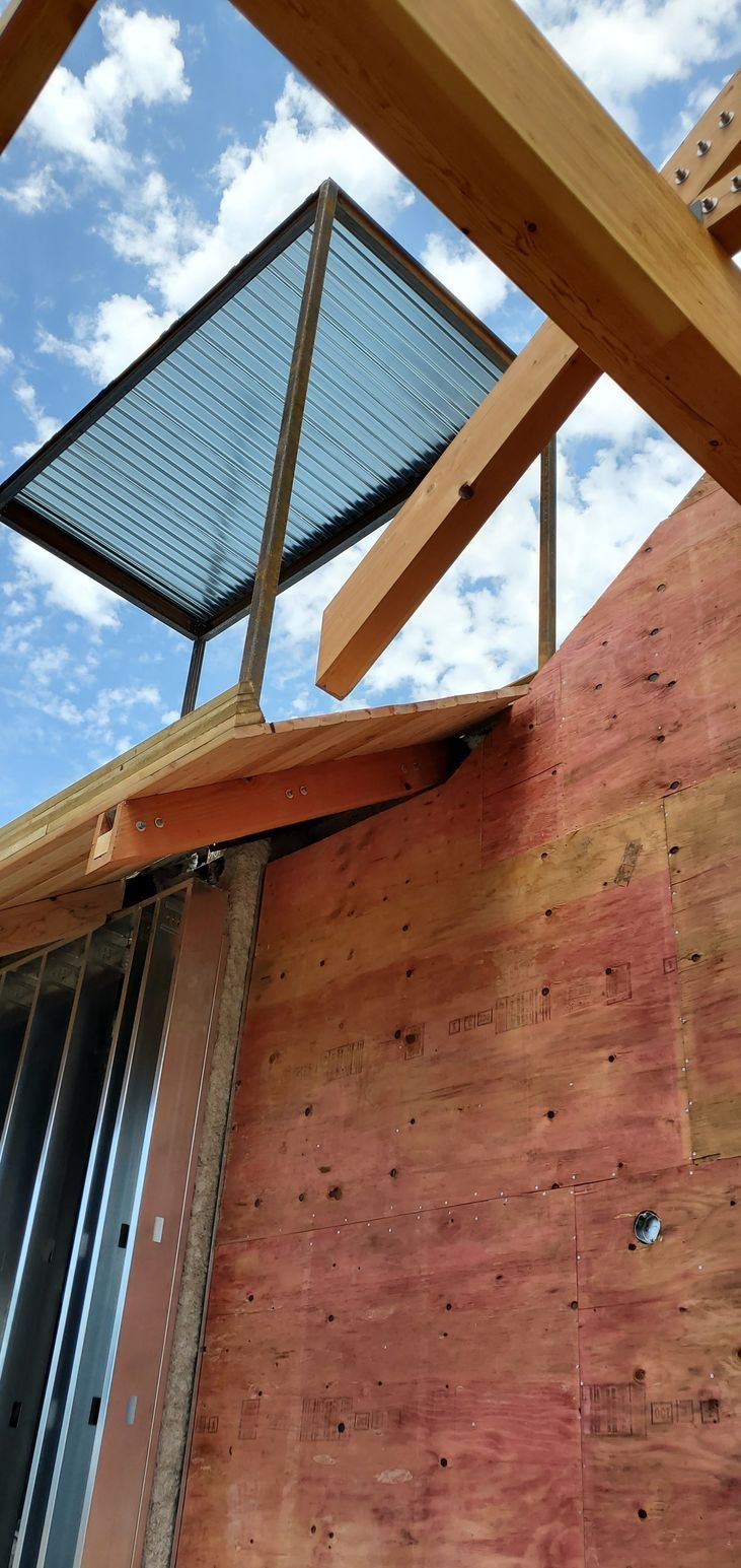 Blue mesh panel mounted above red plywood and wooden beams against a partly cloudy sky
