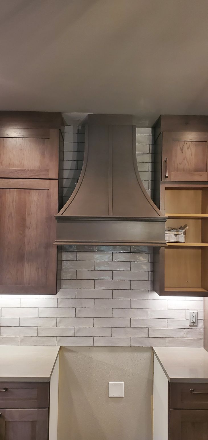 Kitchen with wooden cabinets, white tile backsplash, and a stainless steel range hood above a stove area