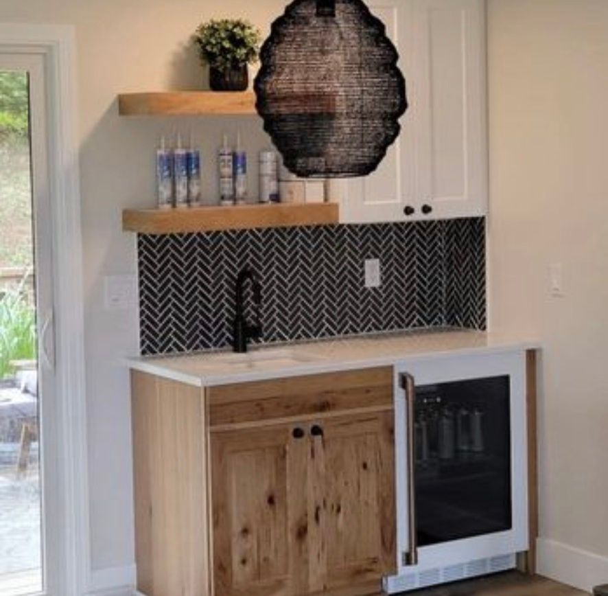 Compact kitchenette with wood and white cabinets, black backsplash, open shelves, and a small undercounter fridge.