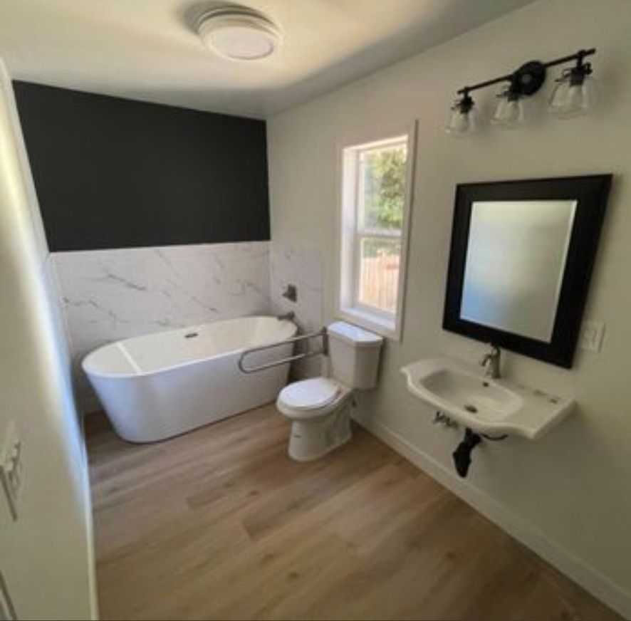 Modern bathroom with freestanding tub, toilet, sink, black-framed mirror, and dark accent wall