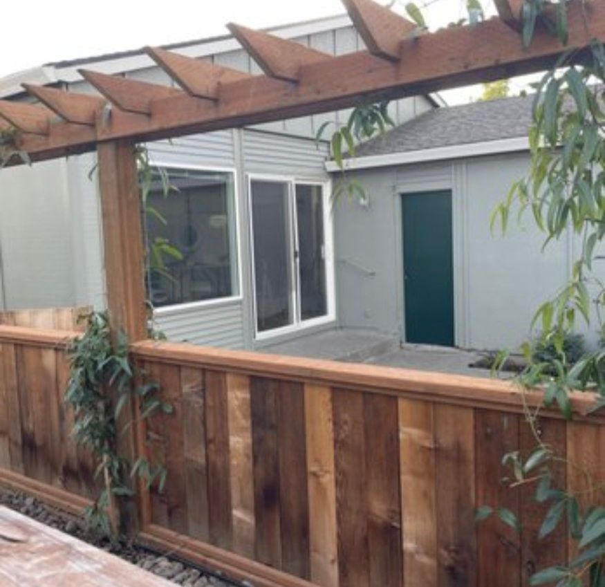 Wooden fence and pergola in a small courtyard with gray siding and green door