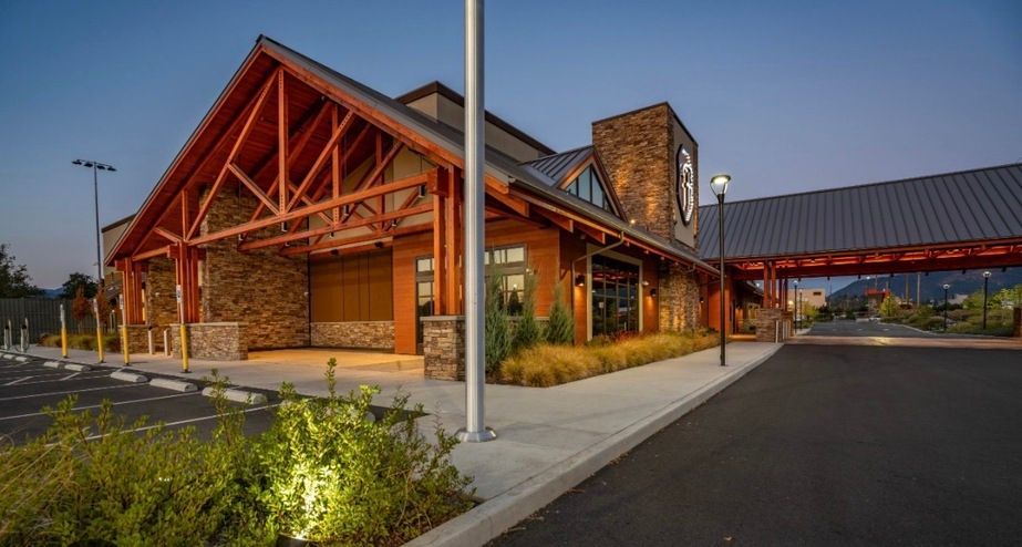Stone and wood building entrance at dusk with red roof trusses, lit landscaping, and a covered walkway