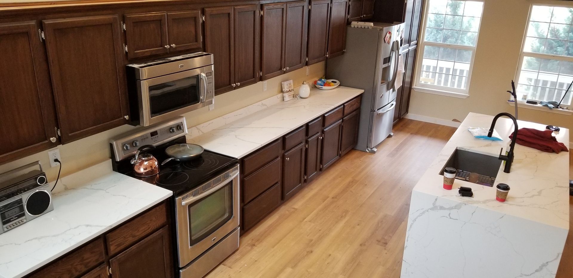 Bright kitchen with dark wood cabinets, stainless stove, and a white island near a window.