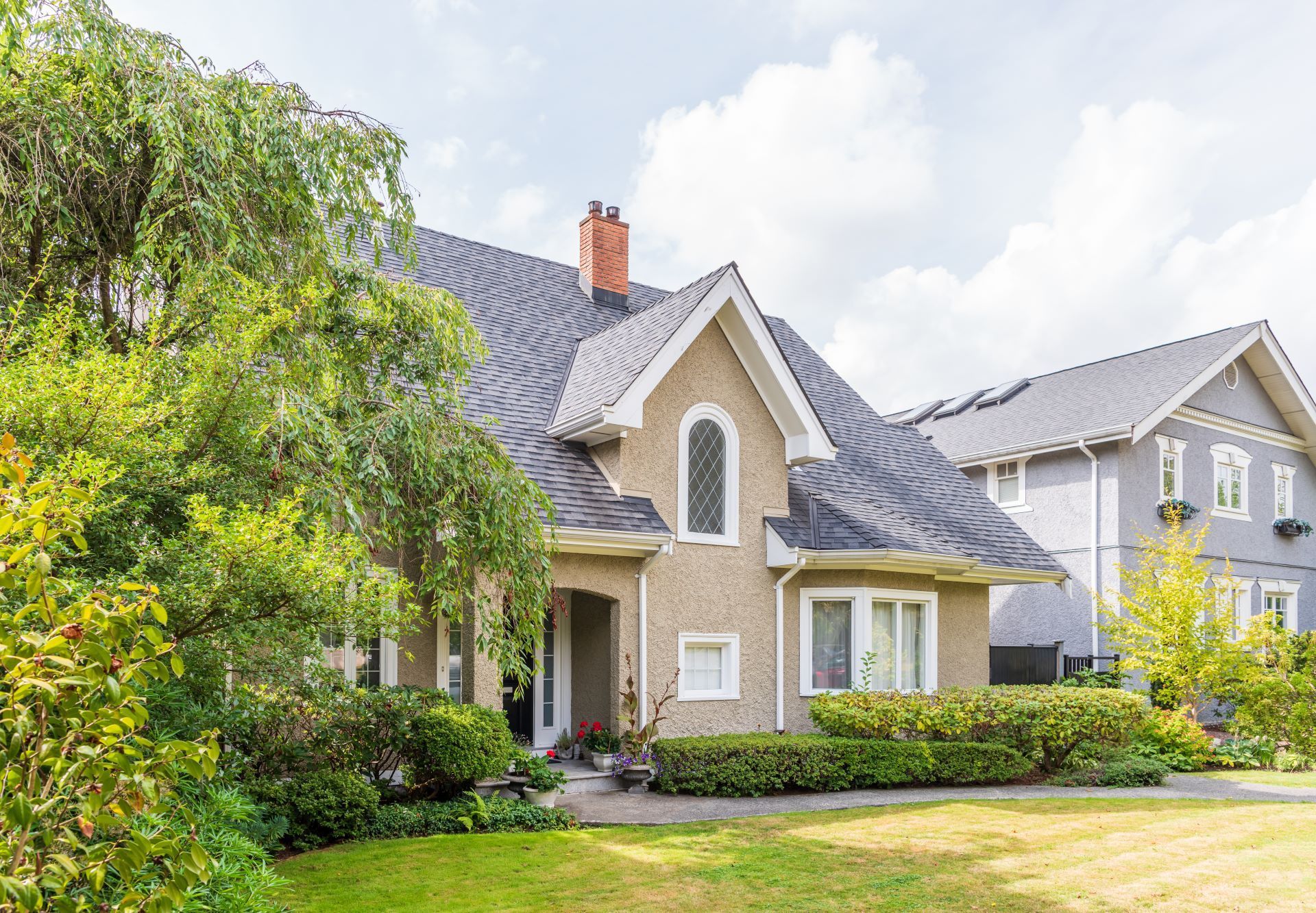 Suburban house with stone facade, gray roof, front porch, and lush green trees and lawn
