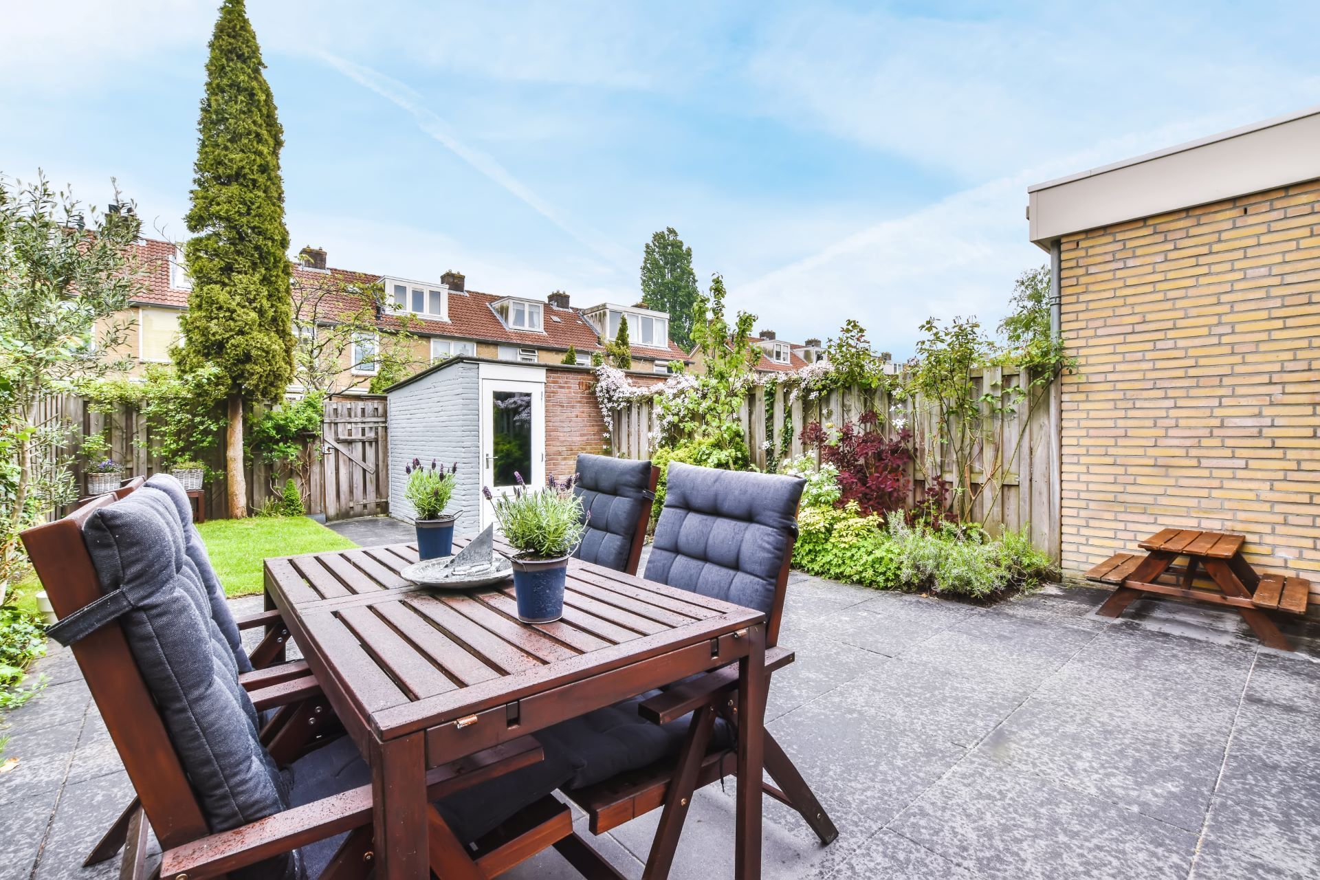 Patio with wooden dining table and cushioned chairs in a bright garden courtyard