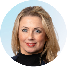 Julie Warner smiling, wearing a black top and blazer, in front of a blue background.
