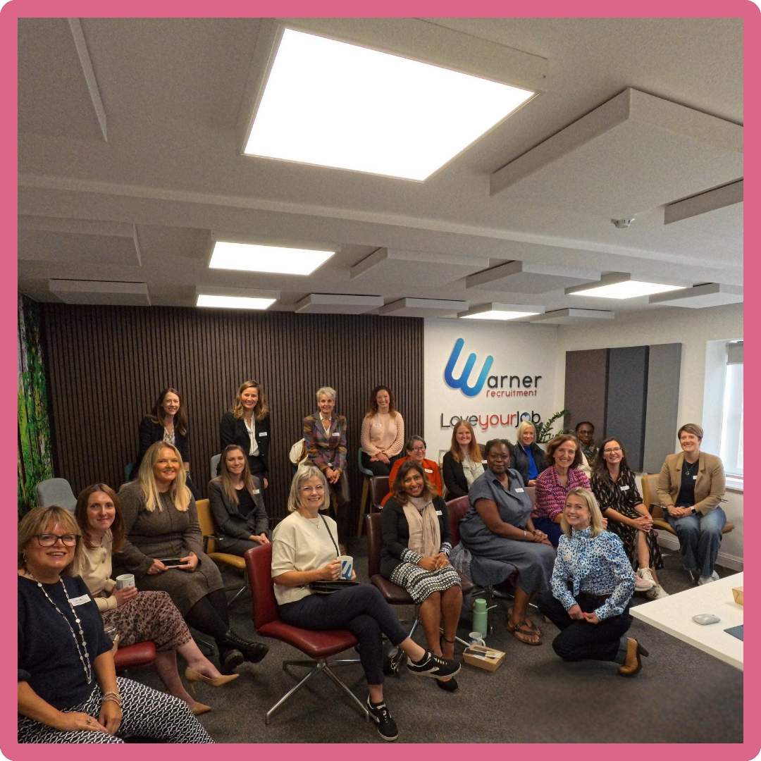 Group of women in an office setting, some seated, some standing, with a 