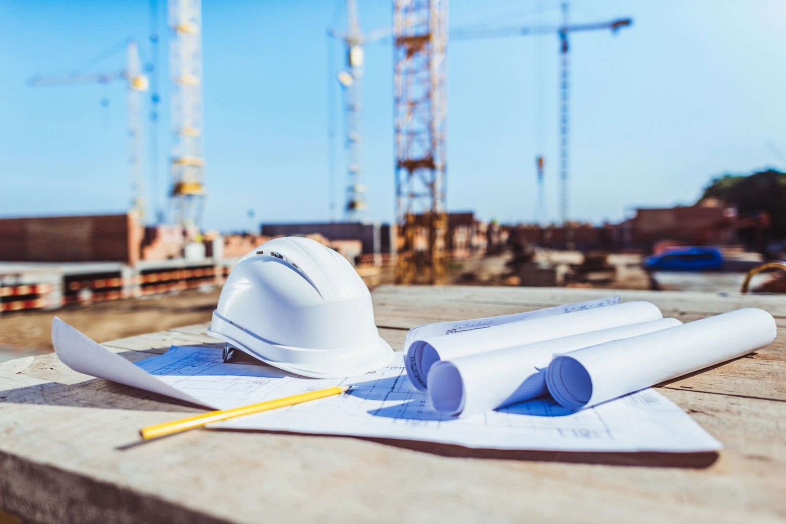 Cantiere con progetto, casco e matita; gru sullo sfondo.