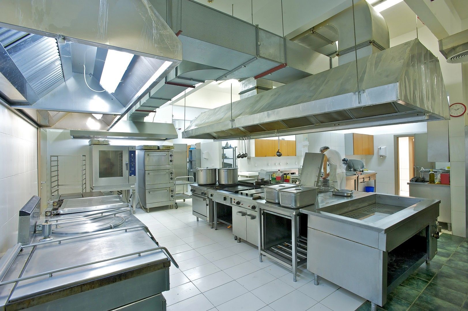 Cucina commerciale con elettrodomestici in acciaio inox e cappe di aspirazione.