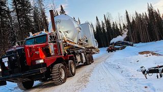A picture of a red bed truck covered in mud and hooked onto a tank.