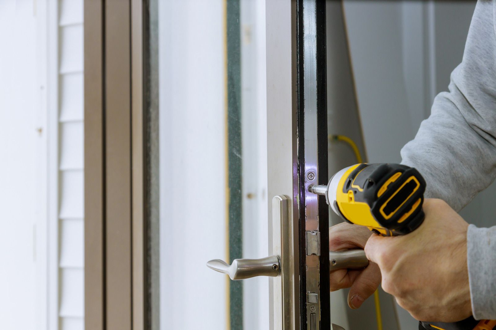 Person using a drill to install a door lock on a white exterior door