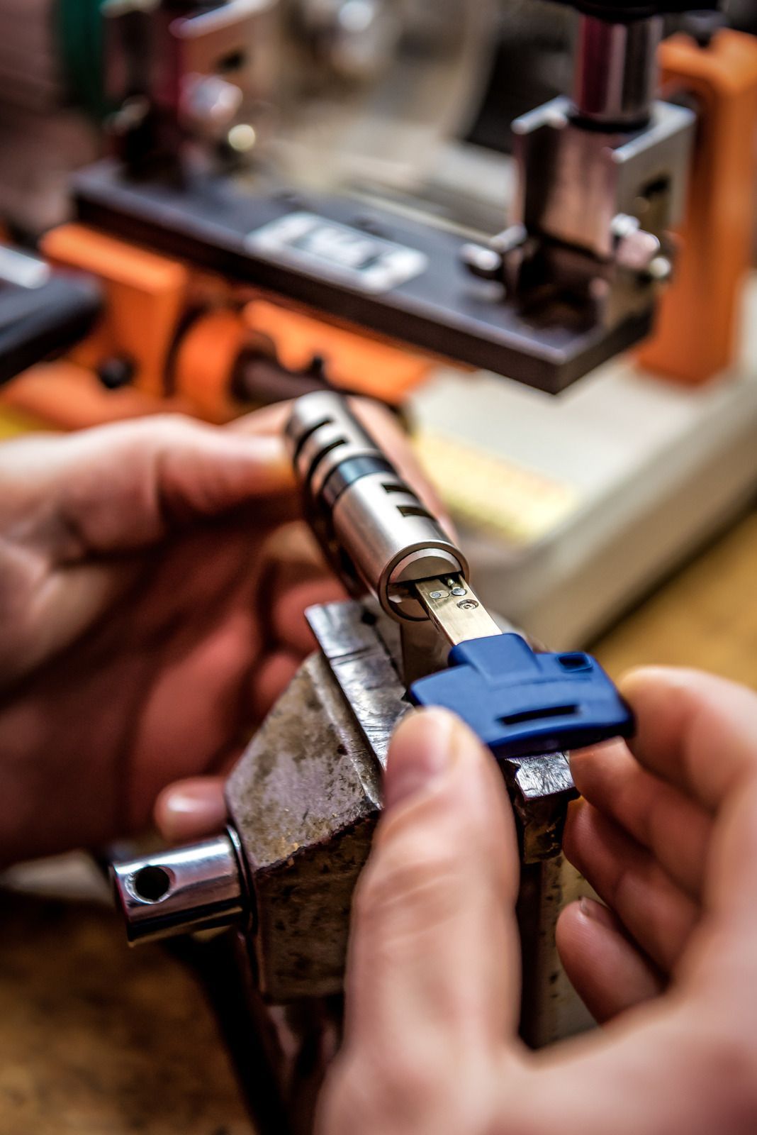 Hands assembling a metal lock cylinder with a blue key, in a workshop.