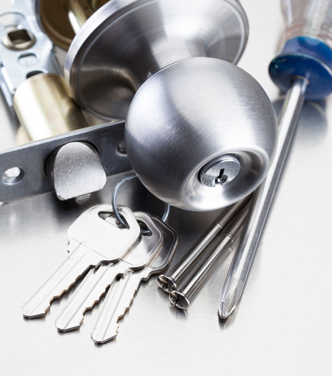 Silver door lock, keys, and lock hardware on a white surface