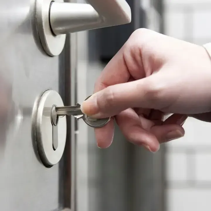 Hand inserting a key into a silver door lock in a close-up view