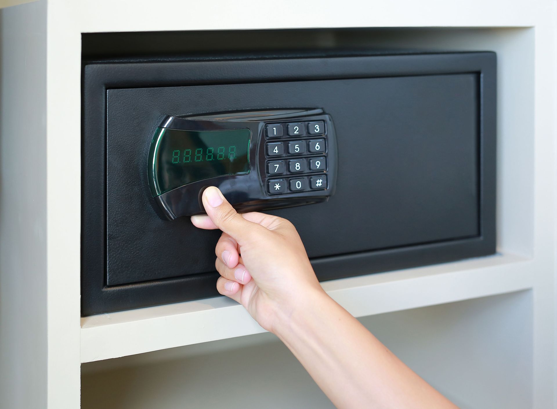 Hand entering PIN on digital hotel safe with black keypad and green display