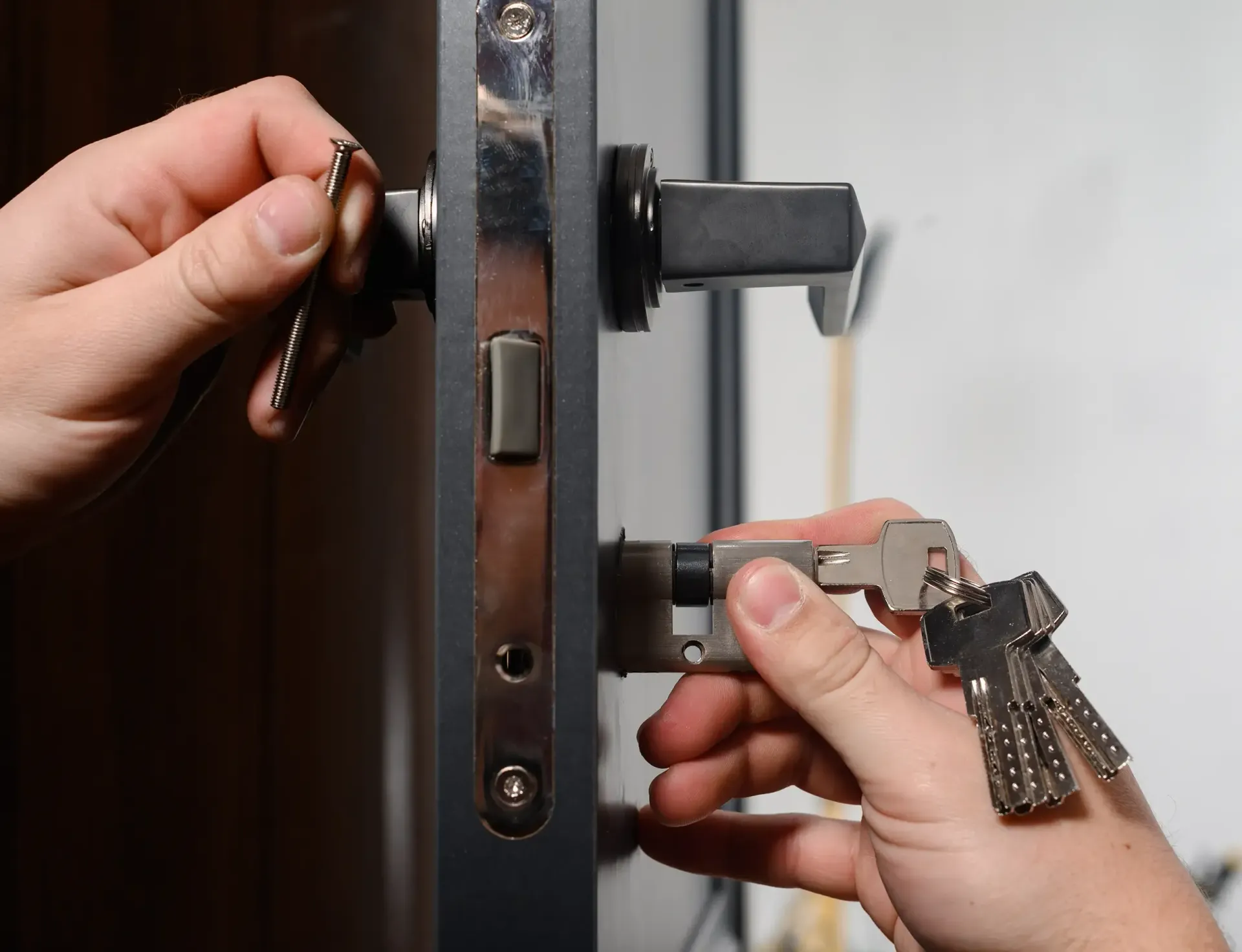 Hands unlocking a black door with a key