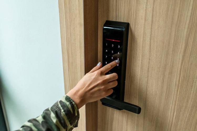 Hand pressing a black digital door lock on a wooden door