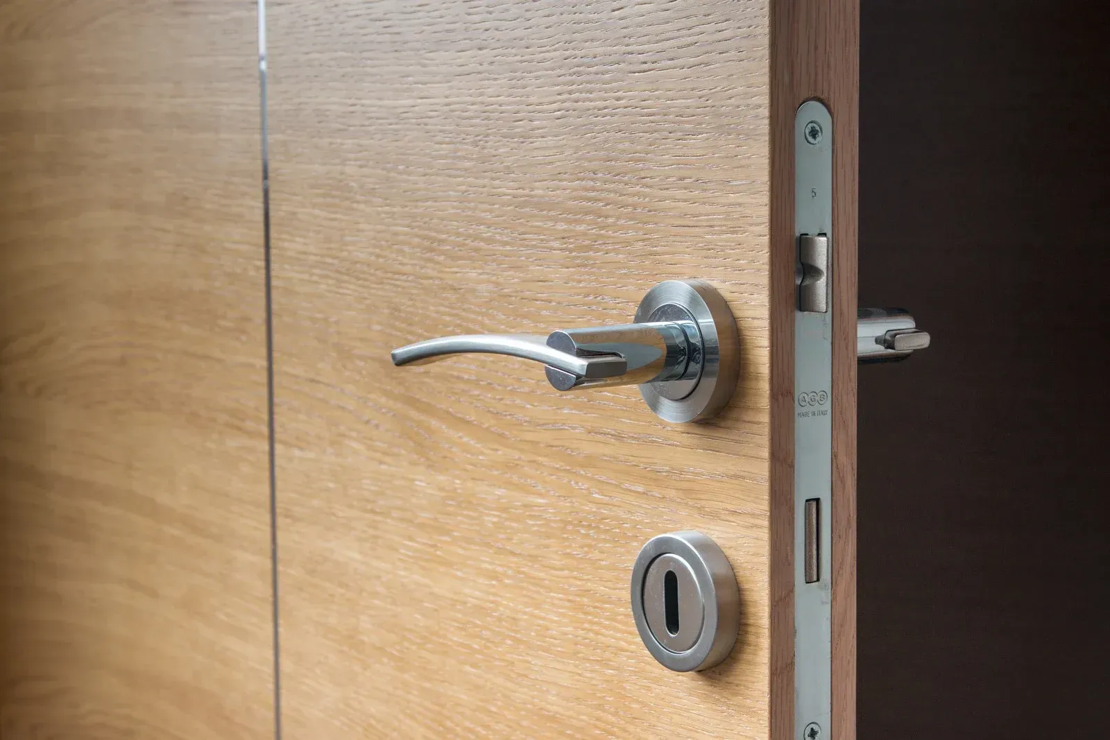 Close-up of a wooden door with a silver handle and lock on the latch side.