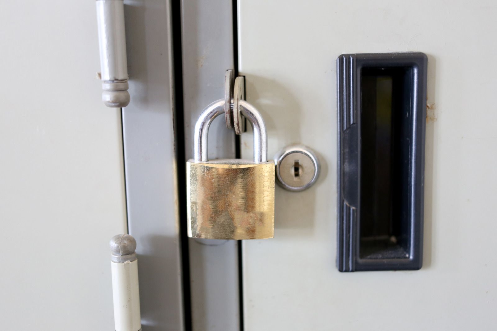 Locked brass padlock on a gray metal door next to a recessed black handle