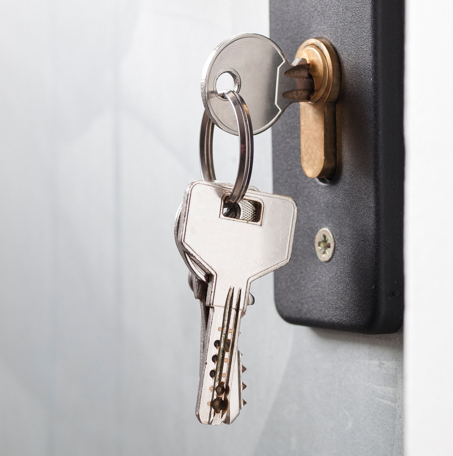 Silver keys on a keyring inserted into a door lock on a white wall