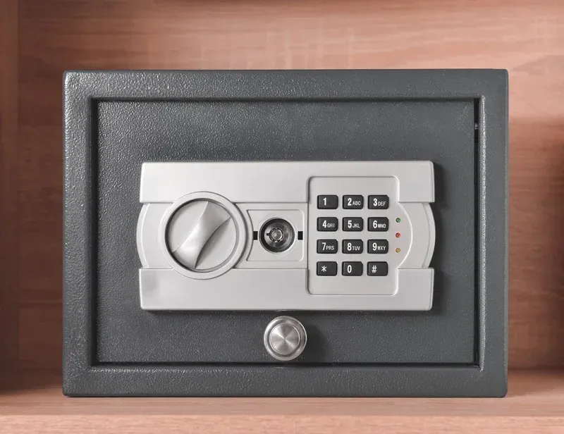 Gray digital safe with keypad and dial on a wooden surface.