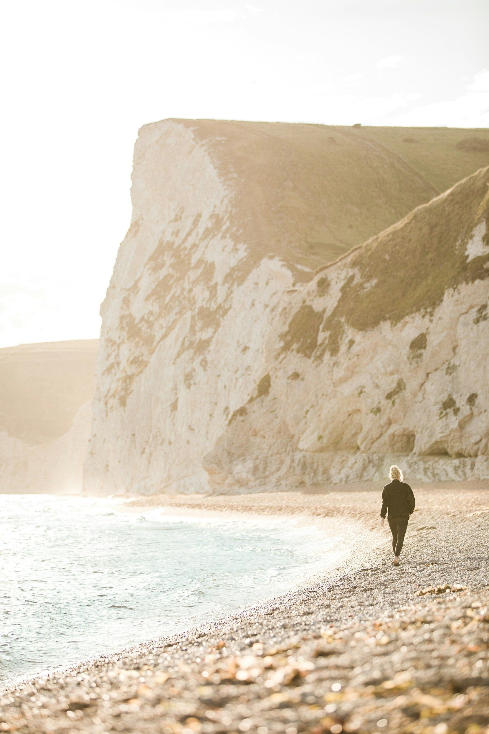 A person is walking along a rocky beach near the ocean.