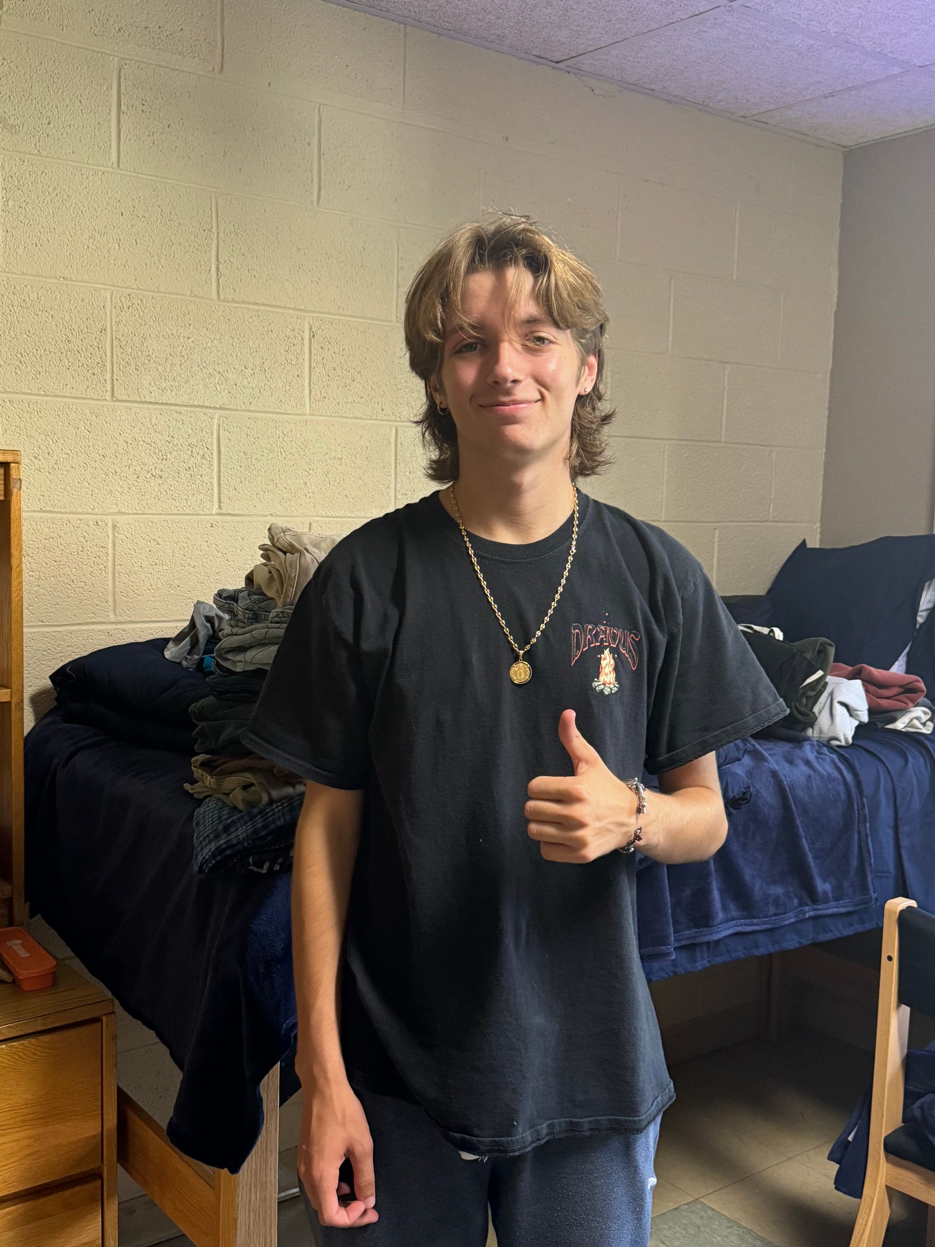 A young man is giving a thumbs up in a dorm room.