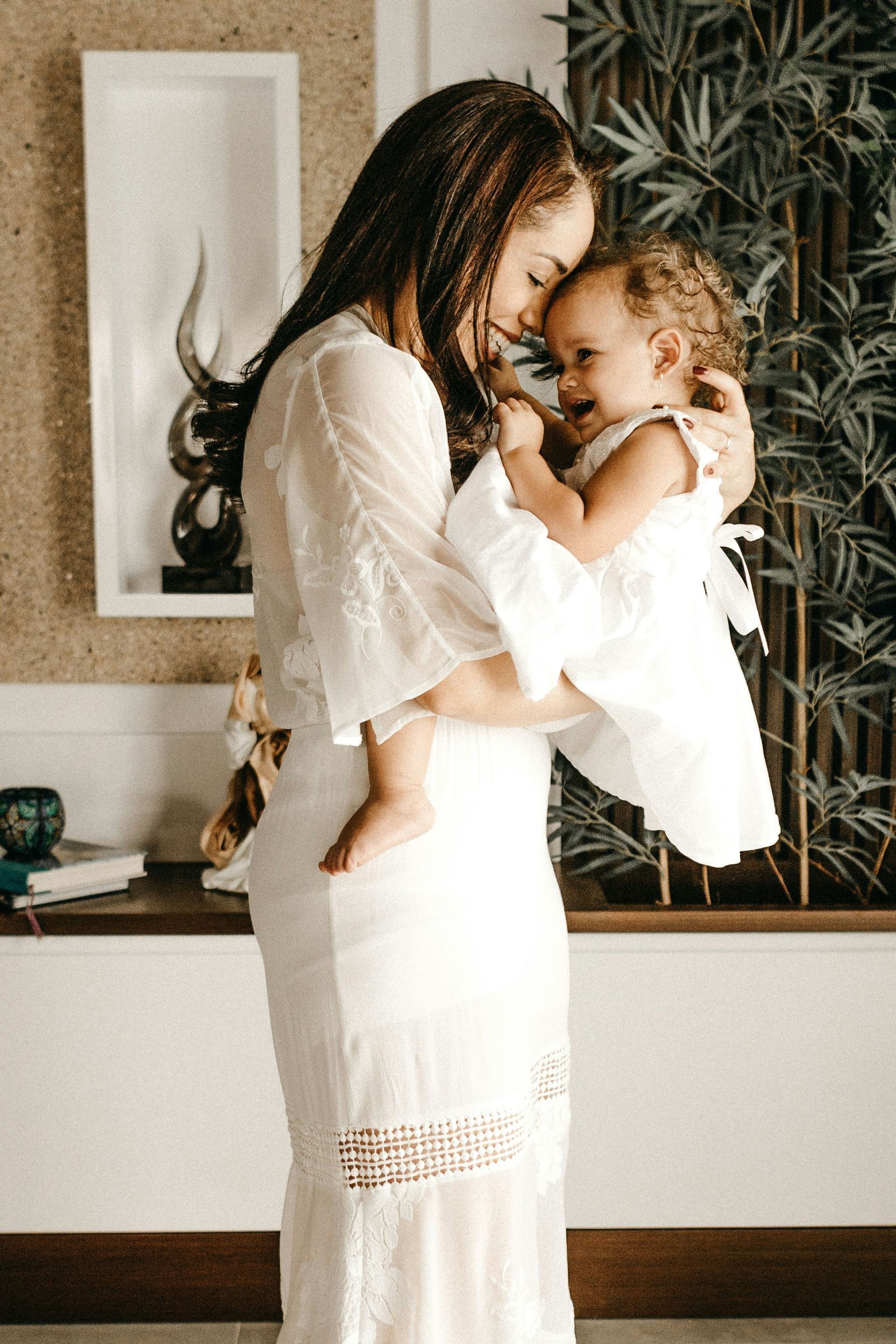 A woman in a white dress is holding a baby in her arms.
