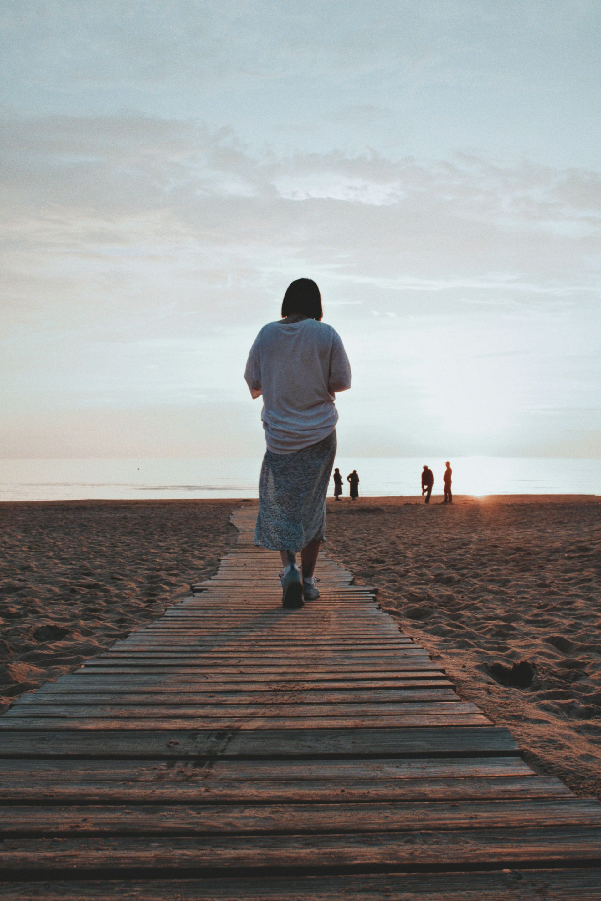 A woman is walking down a wooden walkway to the beach.