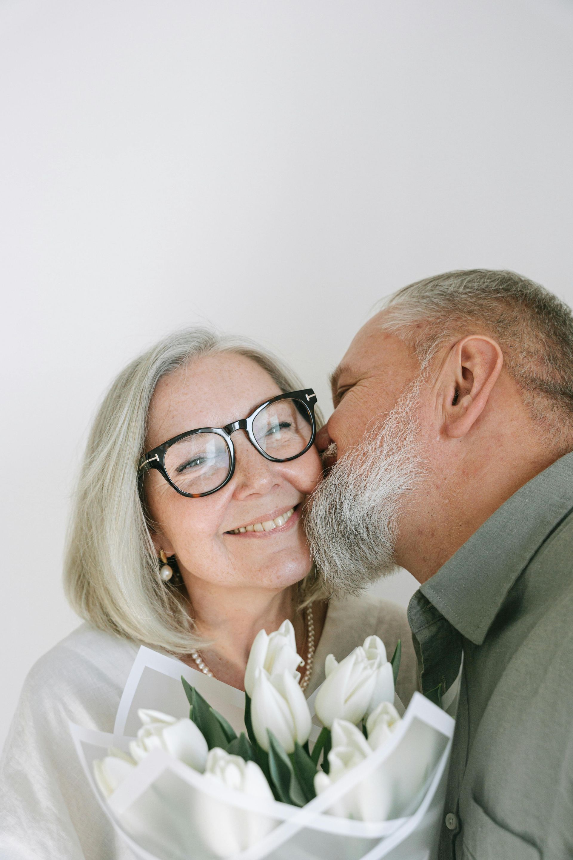 A man is kissing a woman on the cheek while holding a bouquet of flowers.