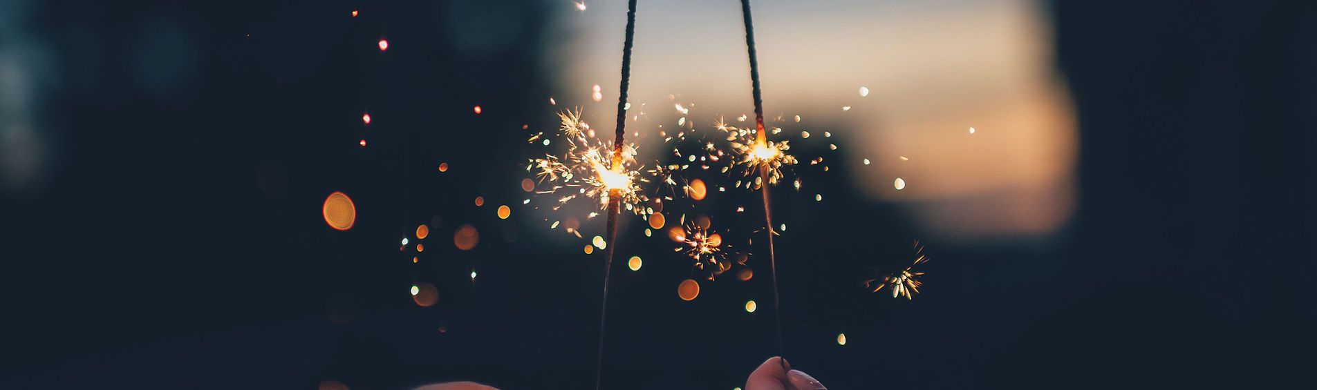 A person is holding sparklers in their hands in the dark.