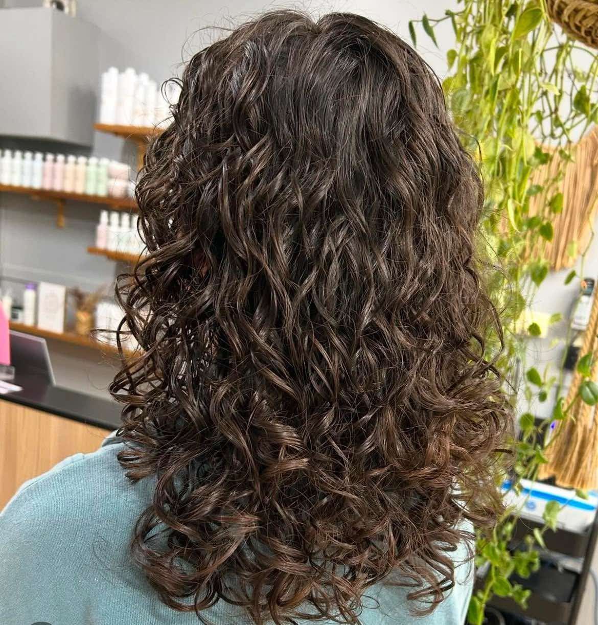 A Woman With Curly Hair Is Standing In Front Of A Shelf โ M & Co Hair Salon In Atherton, QLD