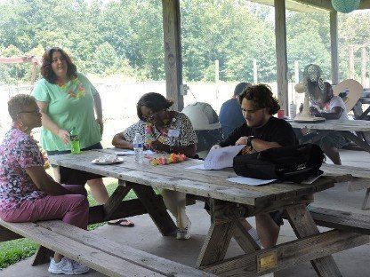 People seated at a picnic table under a pavilion, reading and writing papers.