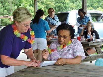 Two women signing papers at a picnic table during an outdoor community event