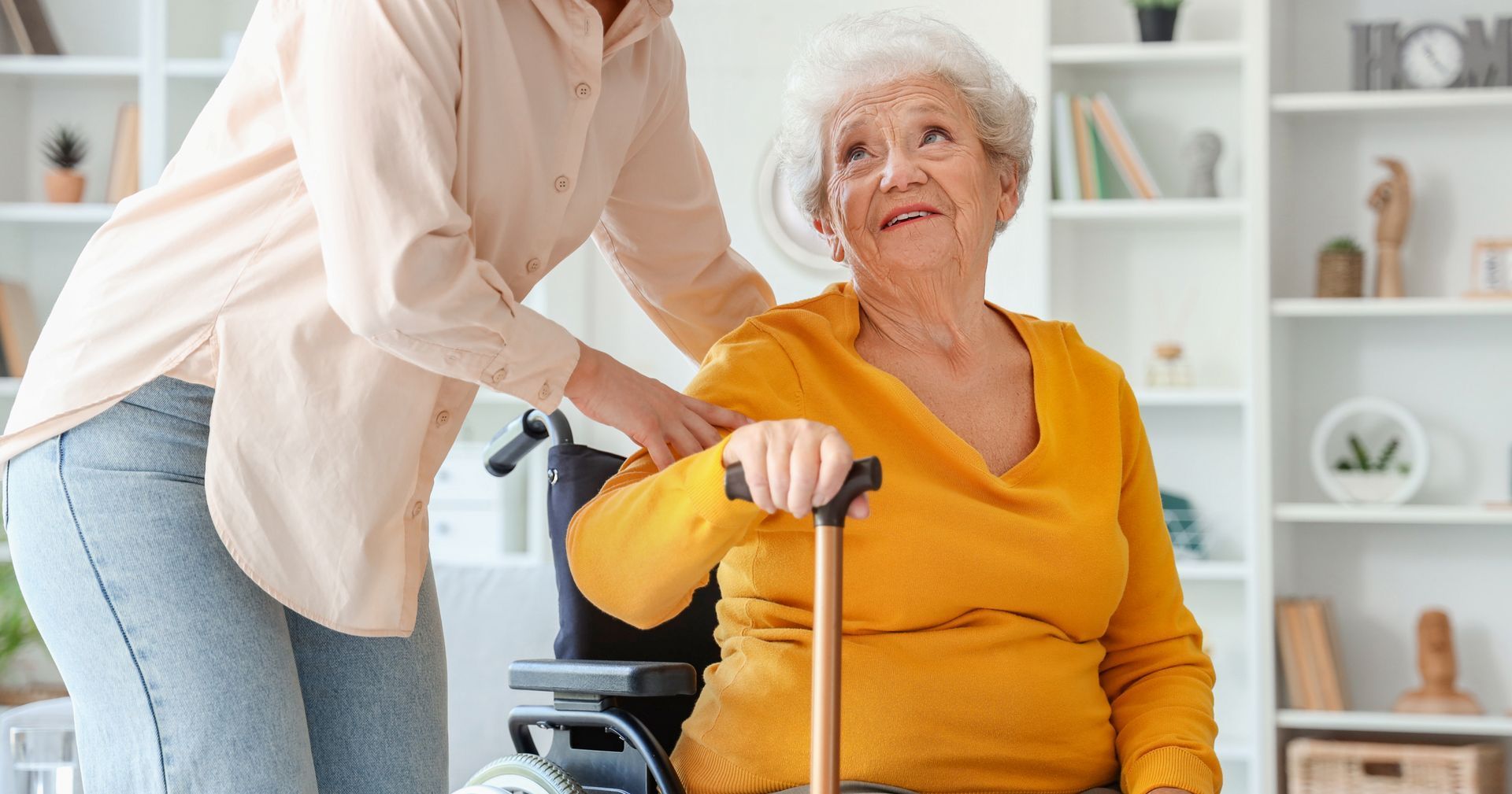 Caregiver assisting a seated woman with a walker in a bright living room
