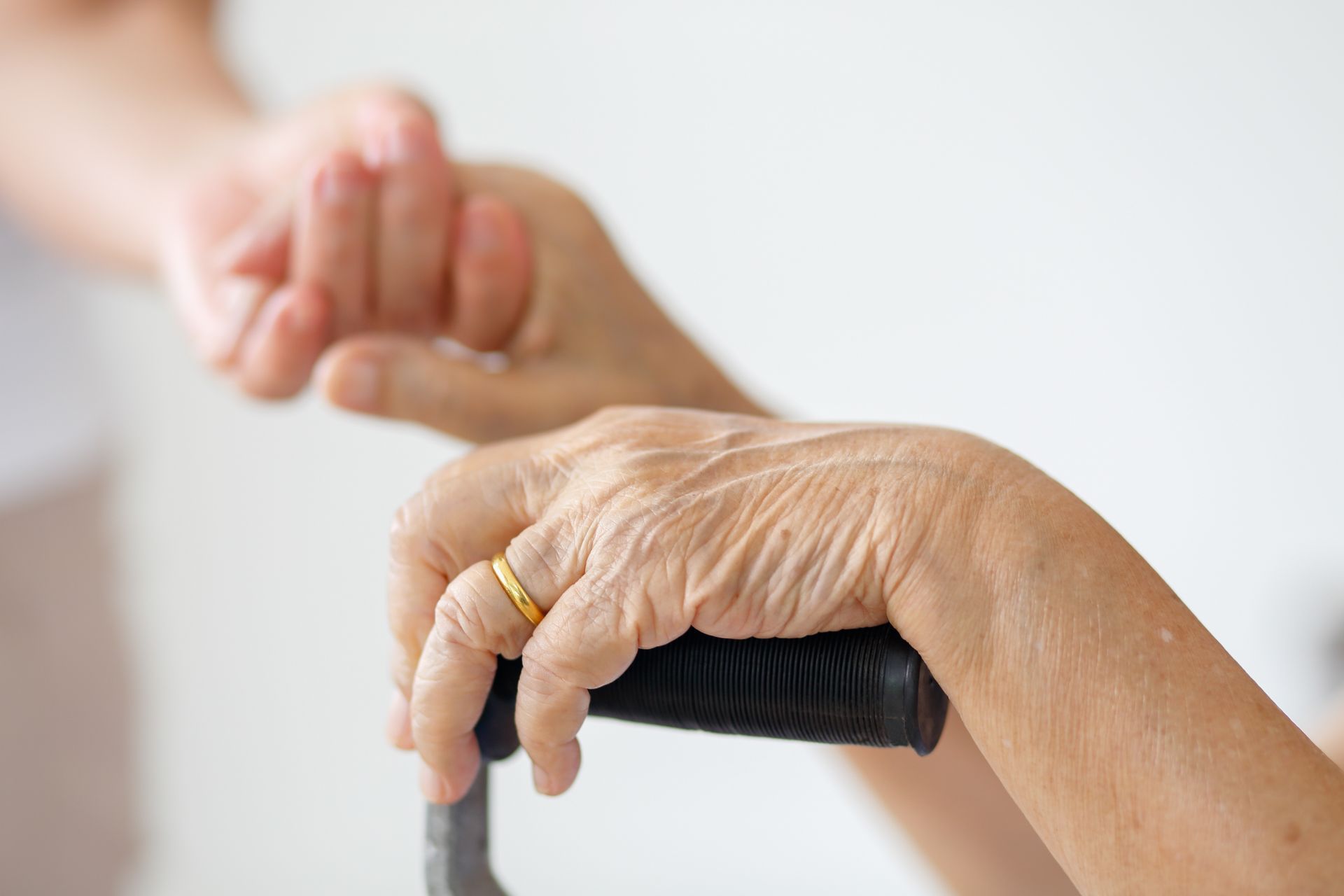 Older hand holding a walker while another hand gently supports it