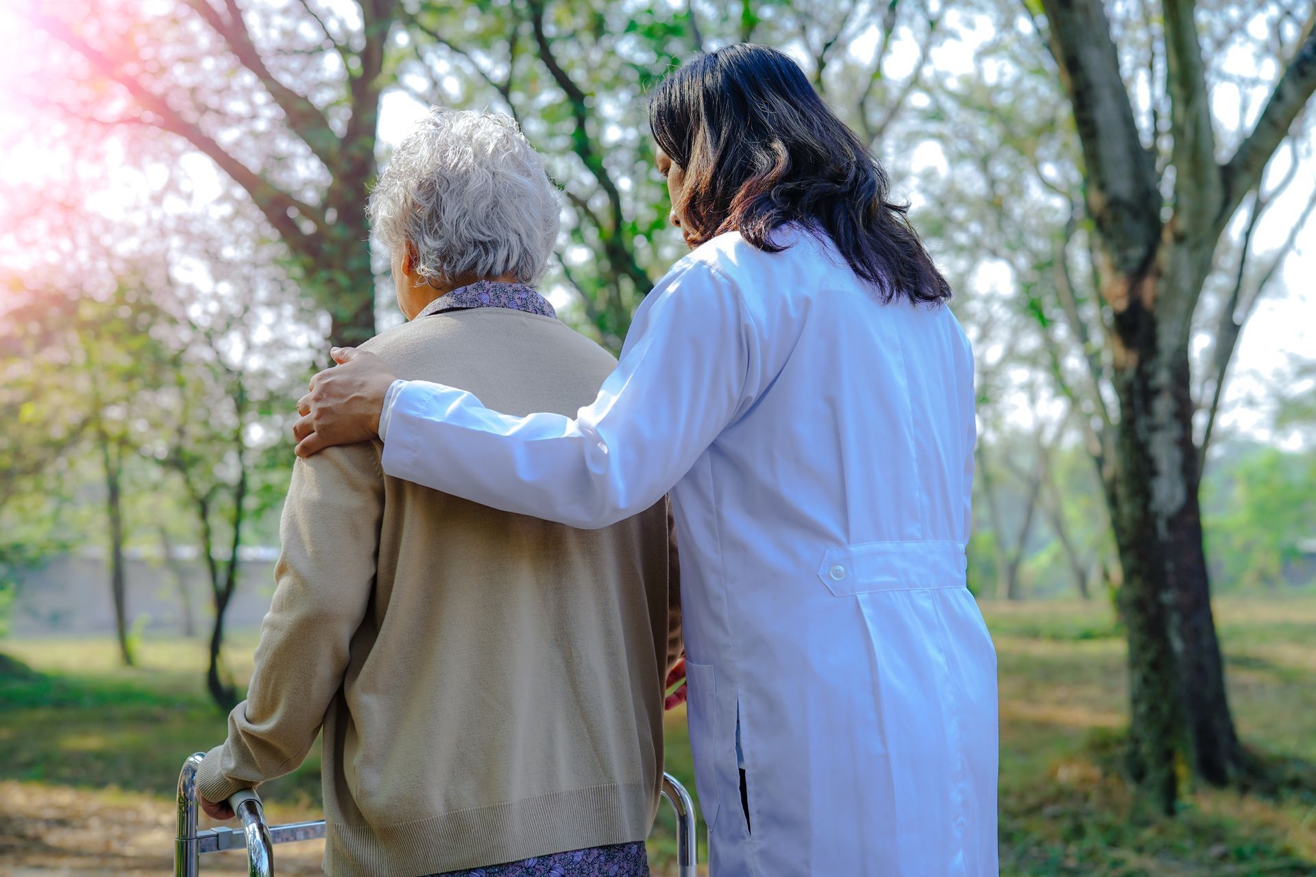 Two people walking outdoors, one with an arm around the other in a sunlit park