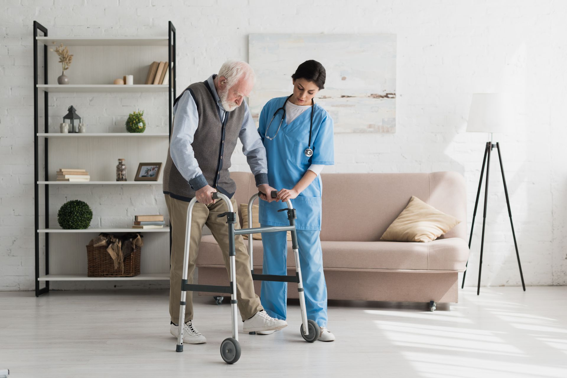 Senior using a walker with help from a caregiver in a bright living room