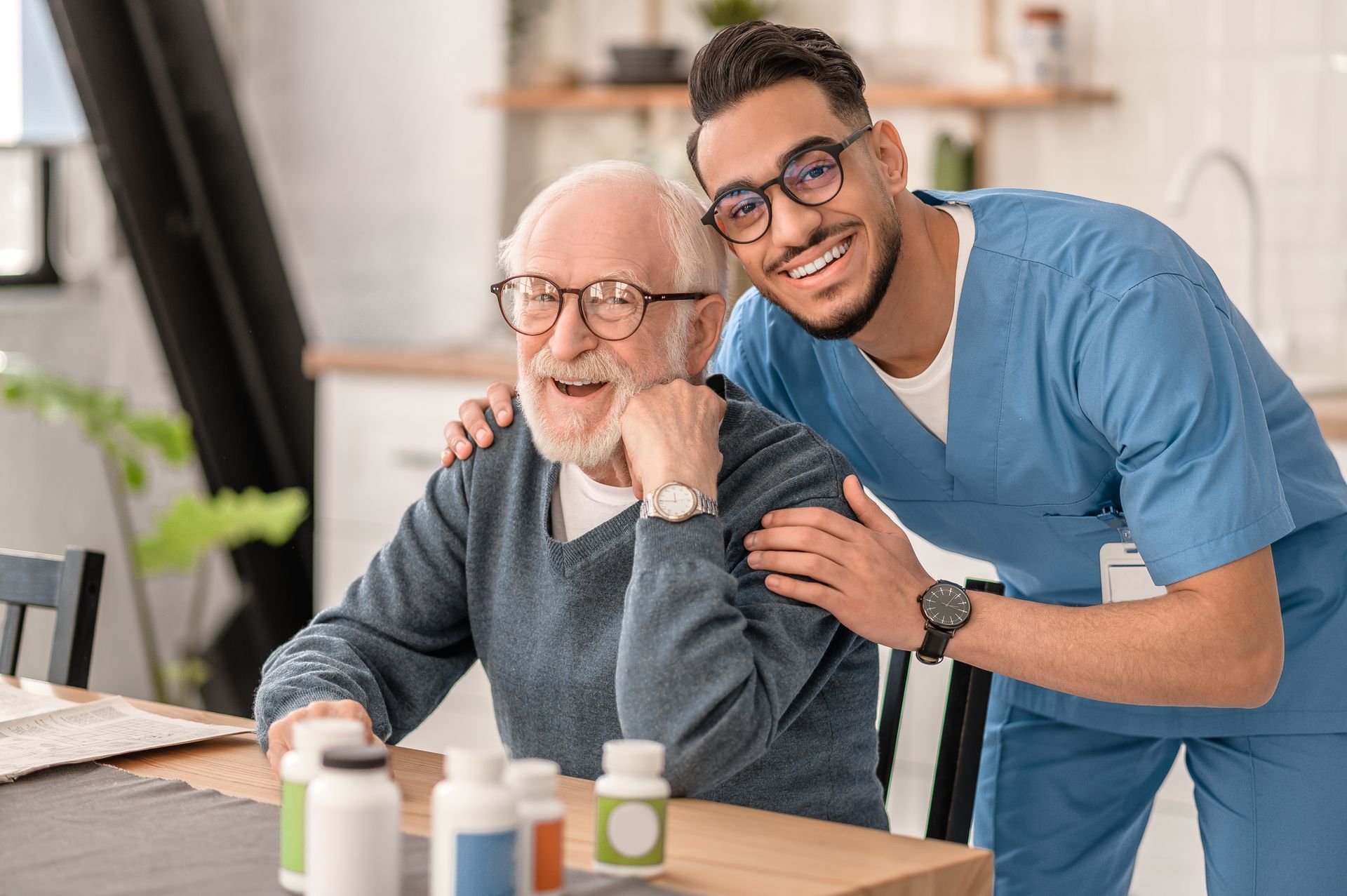 Man and older adult smiling at a table with pill bottles in a bright home setting