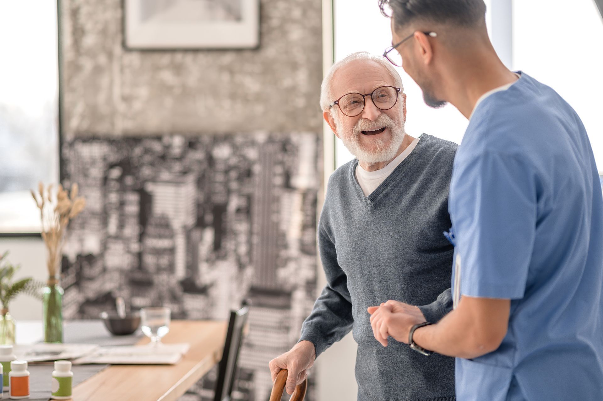Caregiver assisting an elderly person with a walking cane inside a home setting