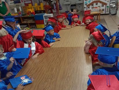 A group of children wearing graduation caps and gowns are sitting at a table.