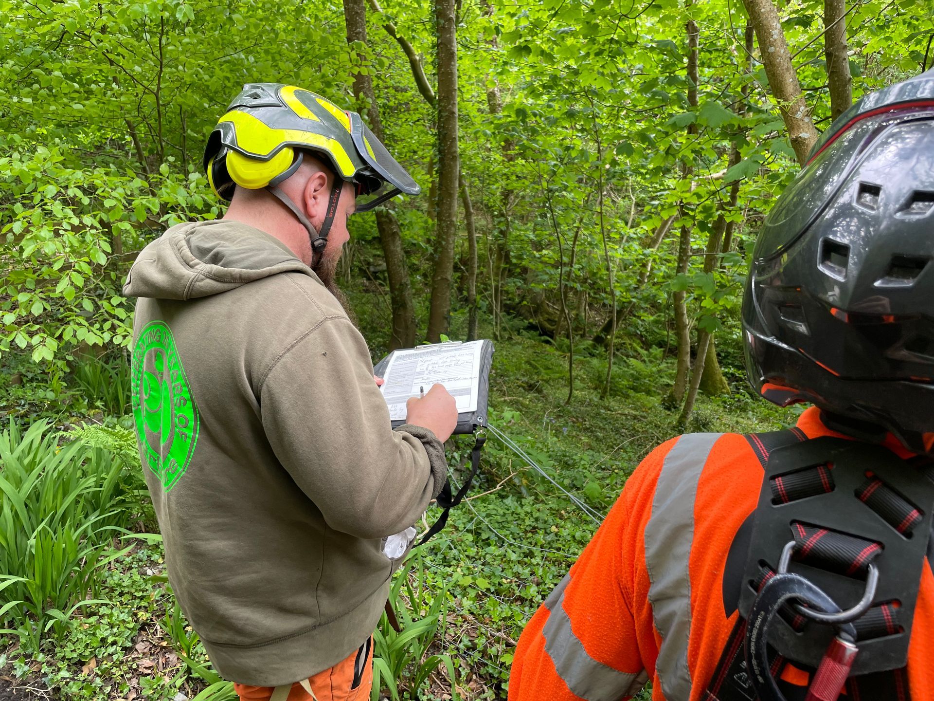 Two cyclists in helmets, one reading a map in a green wooded trail.
