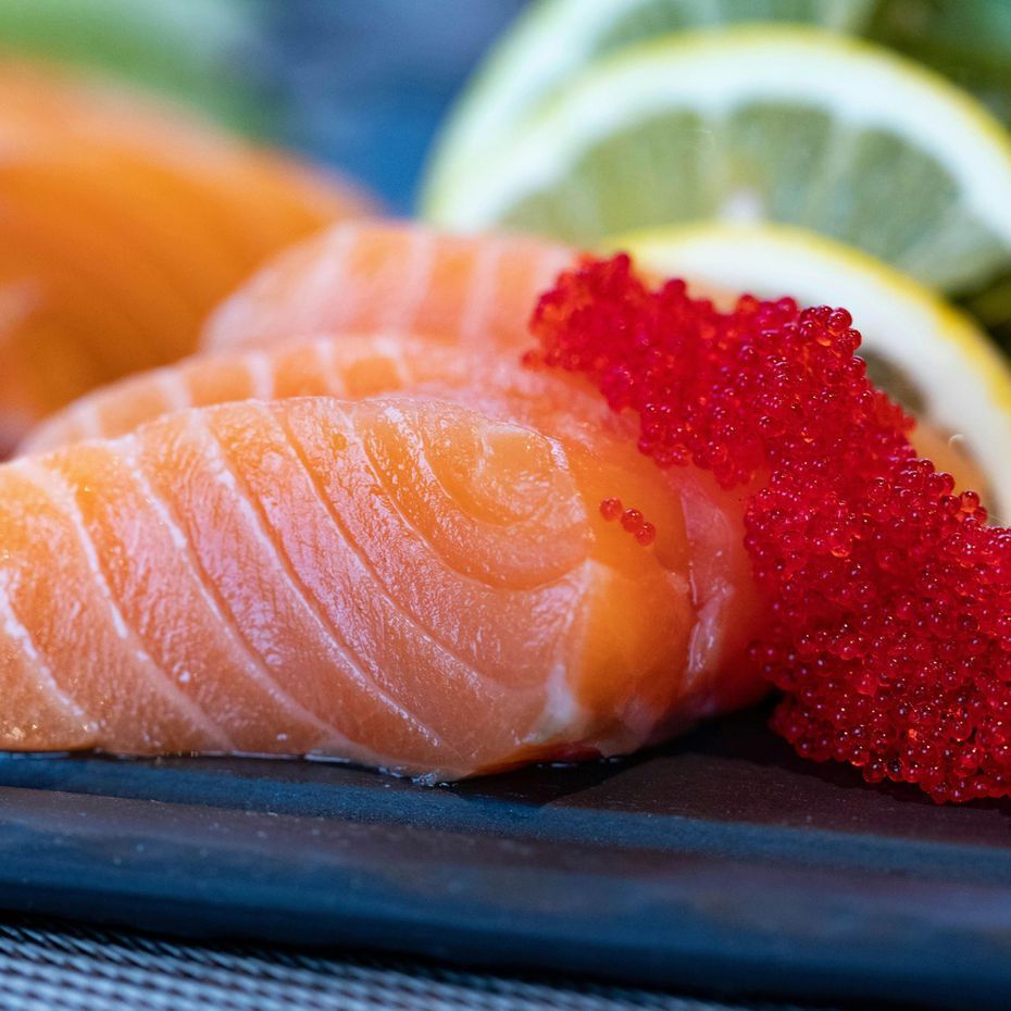Close-up of salmon sashimi with red roe and lemon garnish on a dark plate