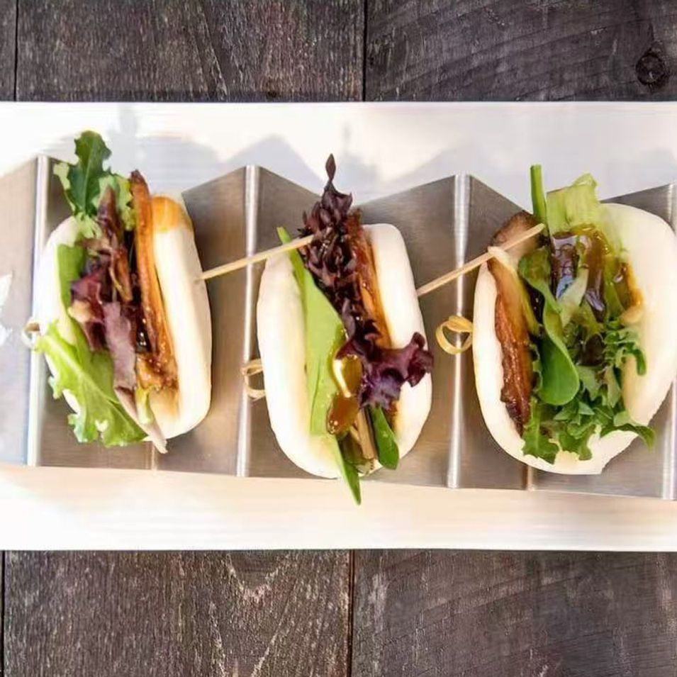 Three mini sandwiches with lettuce and fillings arranged in a tray on a rustic wooden table